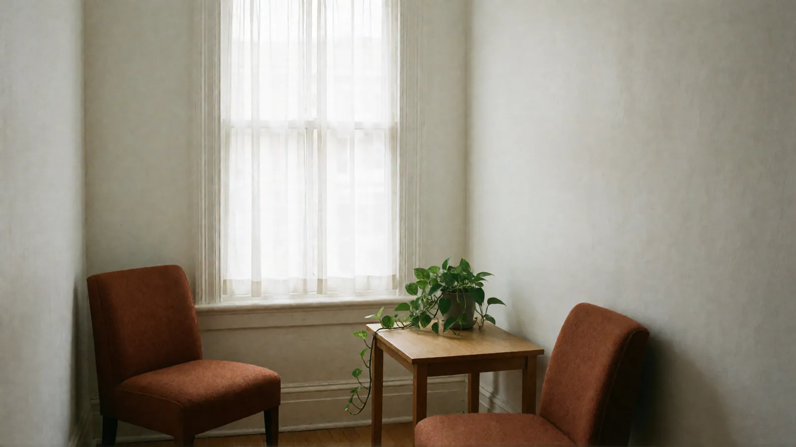 A small room with two rust upholstered chairs angled toward each other and a wooden side table with a trailing pothos plant.